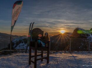 sciatrice seduta sul trono in cima Borno Ski Area e sole che tramonta dietro le montagne